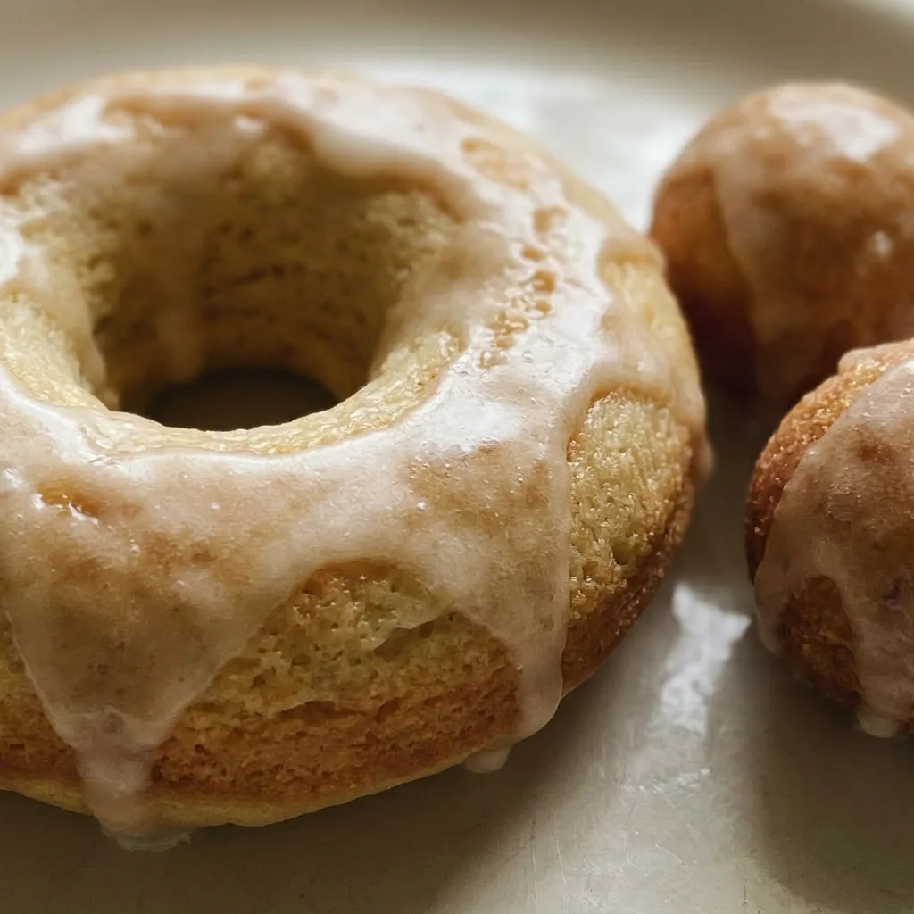 Close view of a glazed donut with rainbow sprinkles, showing its golden-brown surface and airy crumb.