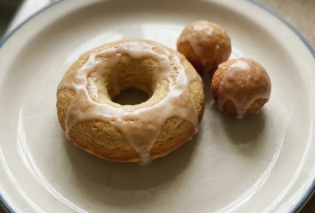 Overhead shot of three round donuts with white glaze and rainbow sprinkles on a dark surface.