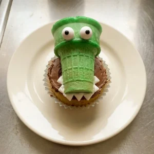 Bird's-eye view of green ice cream cone cupcakes topped with white and chocolate frosting, edible eyeballs, and bubble gum sprinkles.