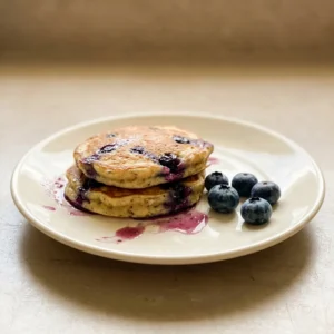 Overhead shot of a stack of three small pancakes topped with fresh blueberries and banana slices.