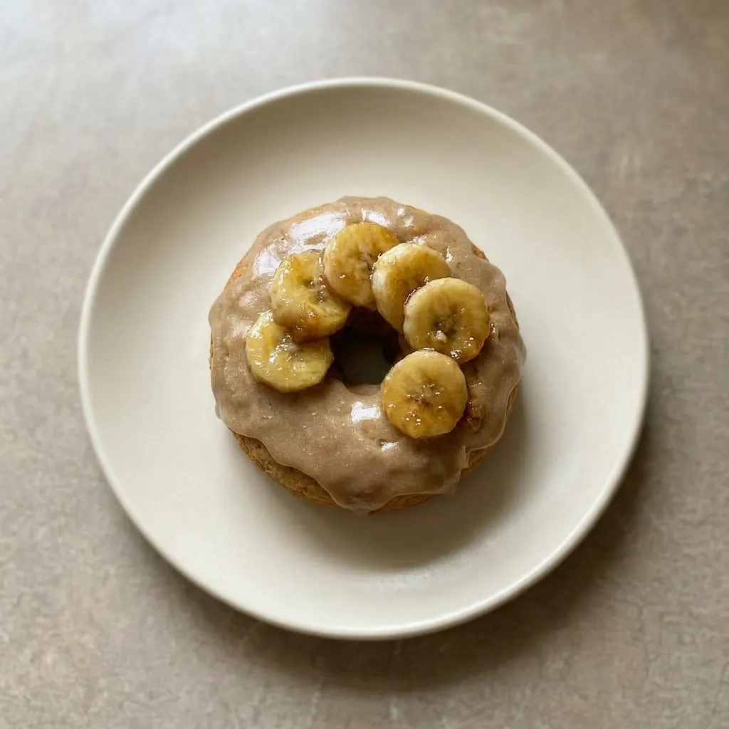 A serving of three donuts stacked, each topped with brown sugar glaze and a banana slice.