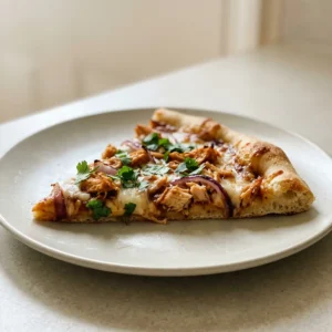 Looking down at a round pizza with BBQ sauce, shredded chicken, mozzarella, red onion, and cilantro.