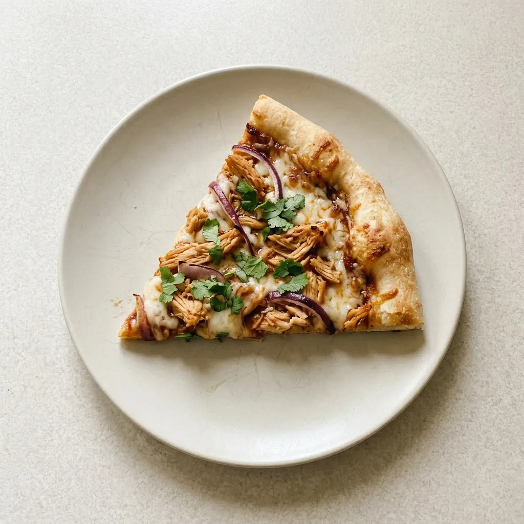 A plate of pizza topped with BBQ sauce, shredded chicken, mozzarella, red onion, and cilantro.