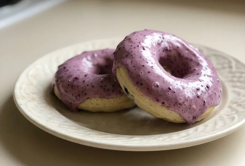 Looking down at a round blueberry cake donut with a glossy blueberry jam glaze and visible blueberries on top.
