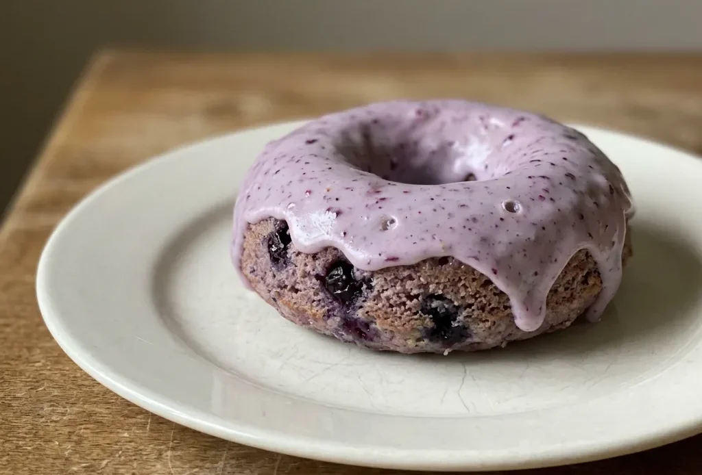 Overhead shot of two blueberry cake donuts with purple berry pieces and a dusting of powdered sugar.