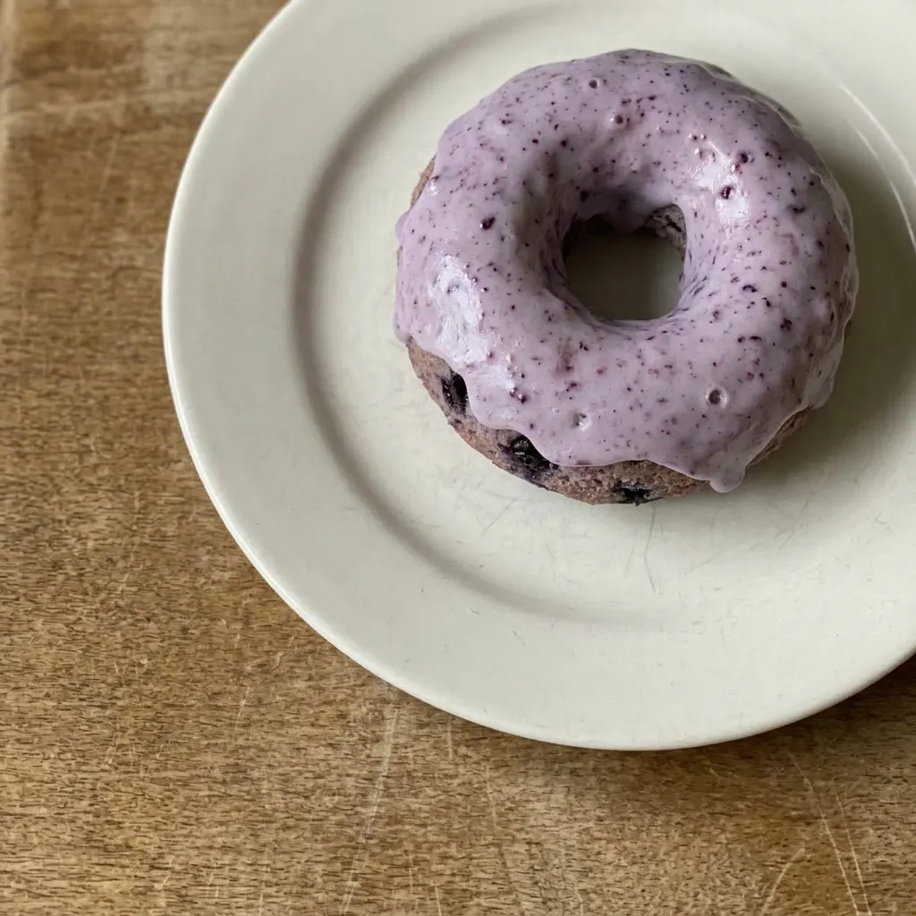 Plated blueberry cake donut topped with powdered sugar, showing wild blueberries embedded in the cake.