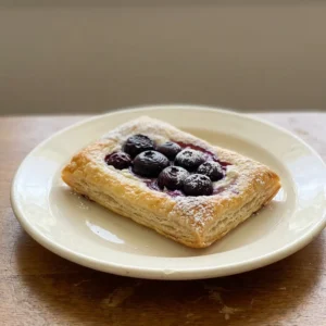 Looking down at a rectangular puff pastry topped with farmer cheese and blueberries, dusted with powdered sugar.