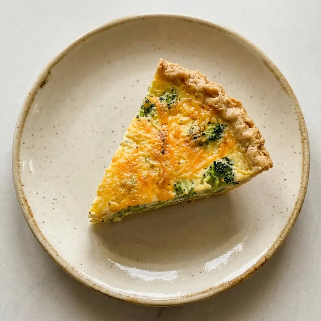 A serving of quiche wedge with broccoli and cheddar cheese, creamy egg custard visible, on a plate.
