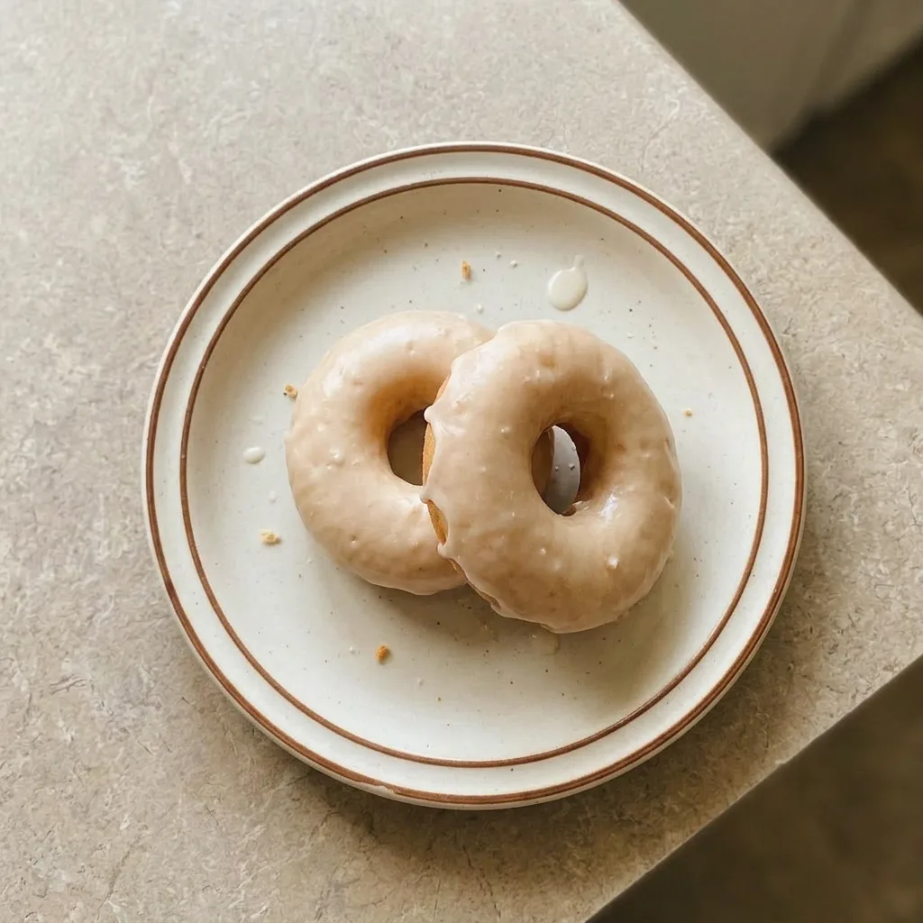 A serving of two glazed buttermilk donuts with vanilla icing and sprinkles.