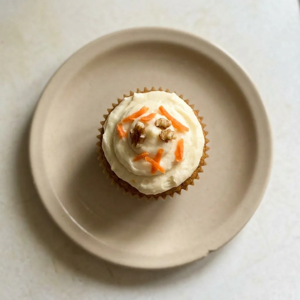 A plate of carrot muffins topped with cream cheese frosting and a dusting of cinnamon, photographed from the side.