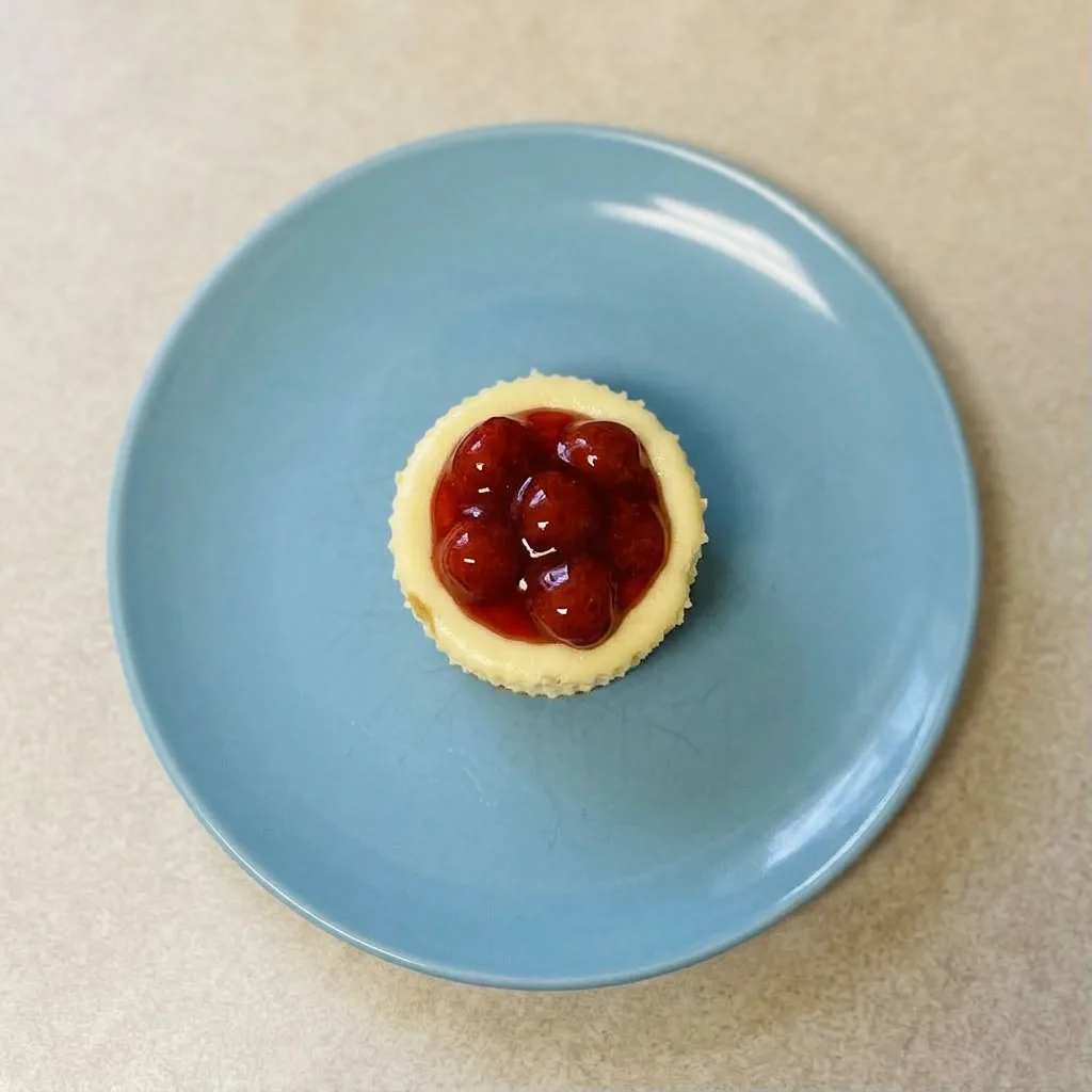 A plate of cheesecake cupcakes each garnished with fresh strawberry and graham cracker pieces.