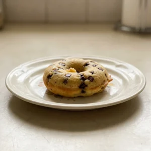 Top-down look at three chocolate chip donuts on a dark surface, each ring dotted with mini chocolate chips.