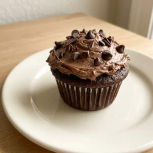 Looking down at three chocolate cupcakes with swirled cocoa frosting and a dusting of cocoa powder.