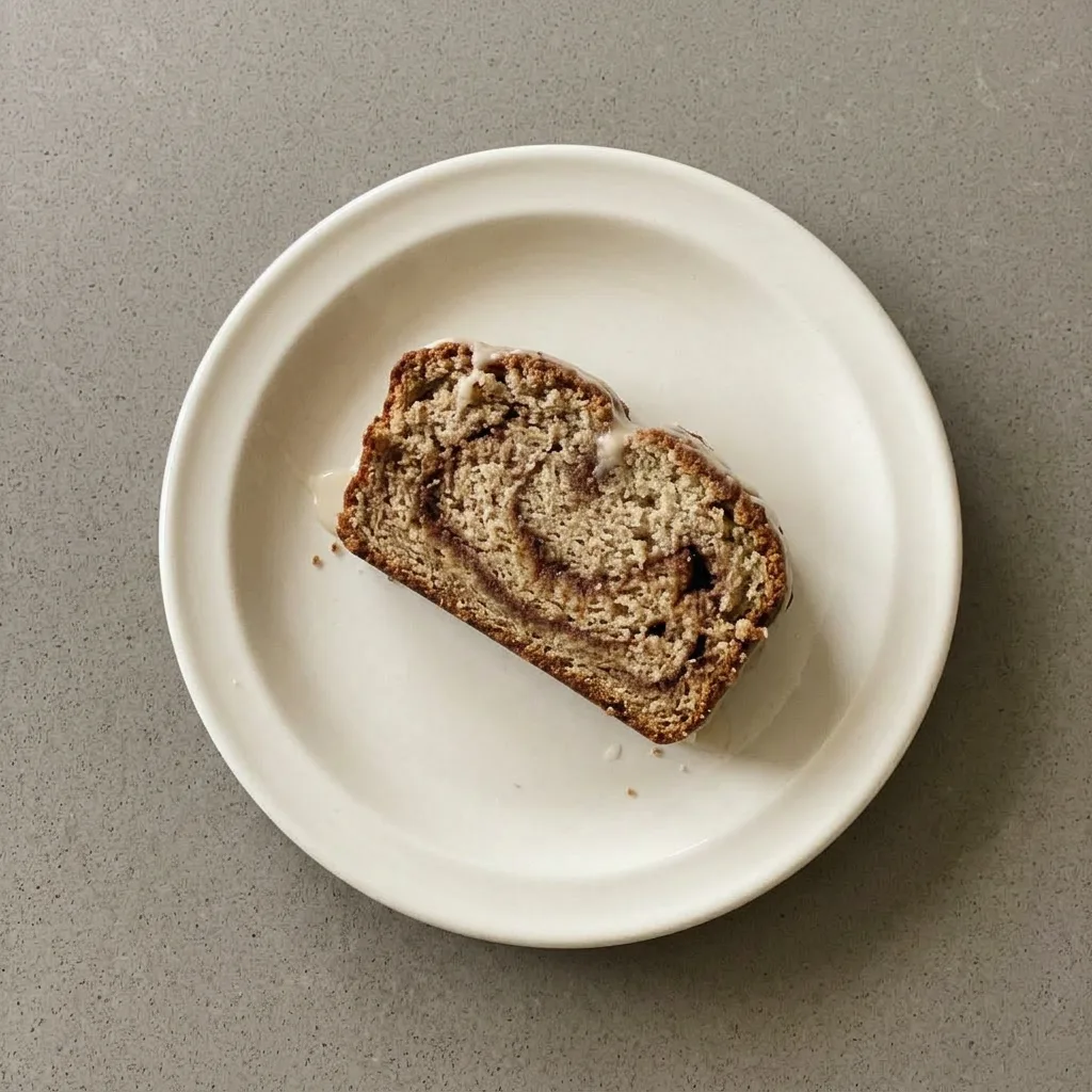 A serving of banana bread topped with a ribbon of icing and visible banana pieces, sliced in half.