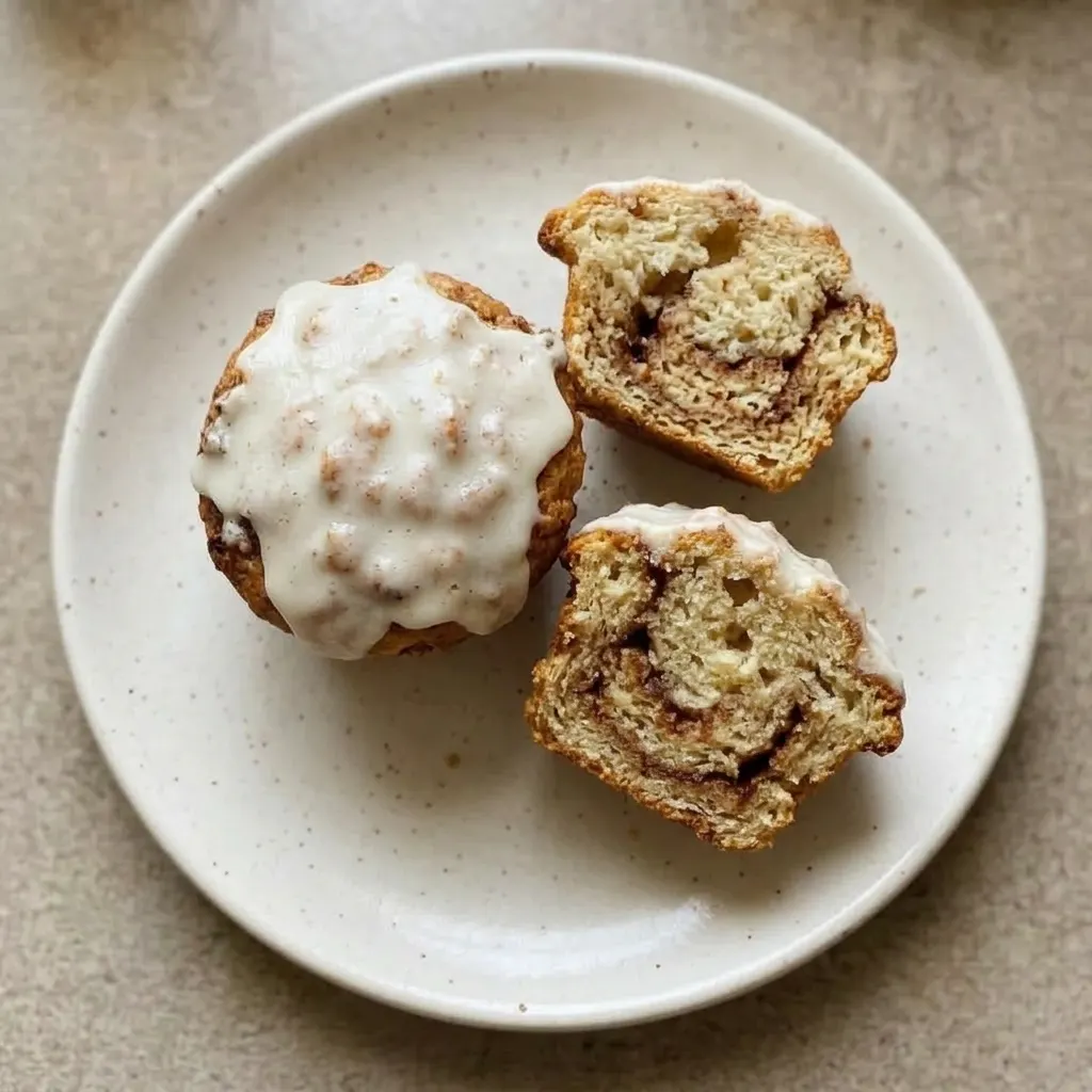 A plate of three muffins with cream cheese icing pooling on top and cinnamon specks visible.