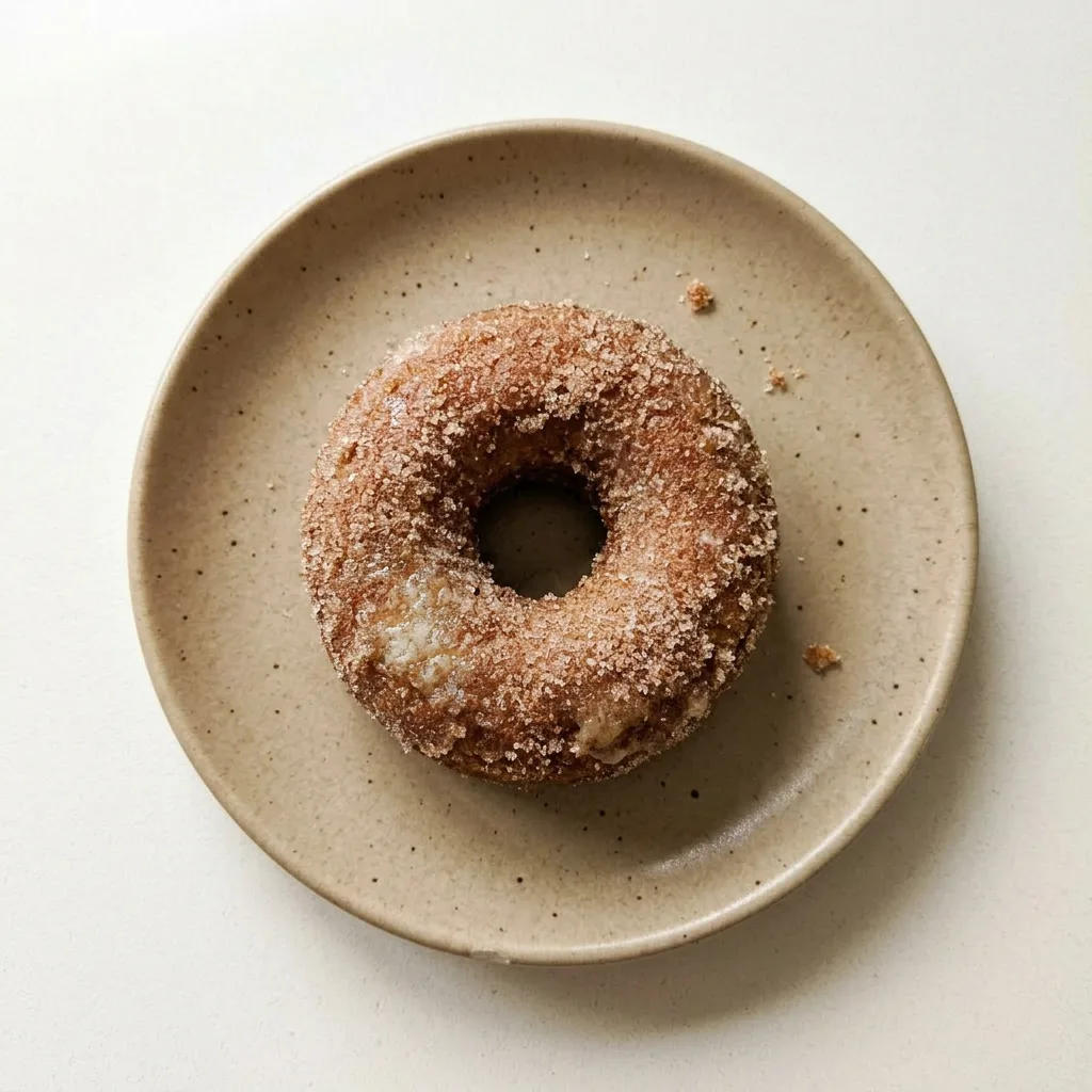A plate of two donuts dusted with cinnamon sugar, one with a bite taken out, revealing the interior.