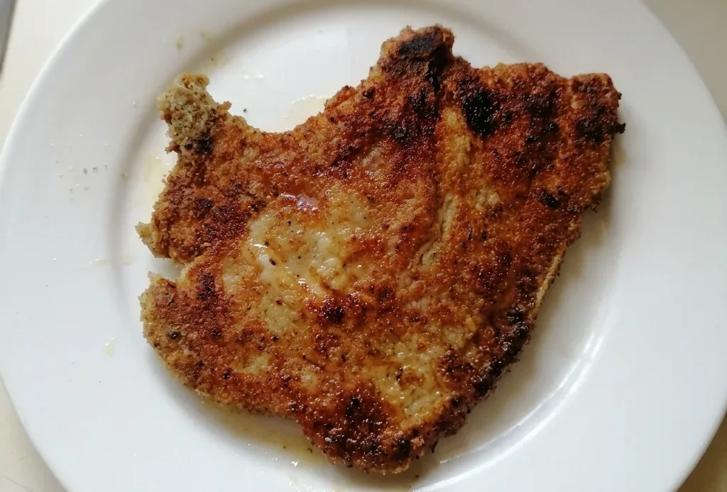 Overhead shot of two breaded pork chops with golden brown crust and herb flecks.