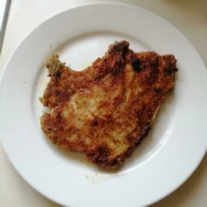 Overhead shot of two breaded pork chops with golden brown crust and herb flecks.