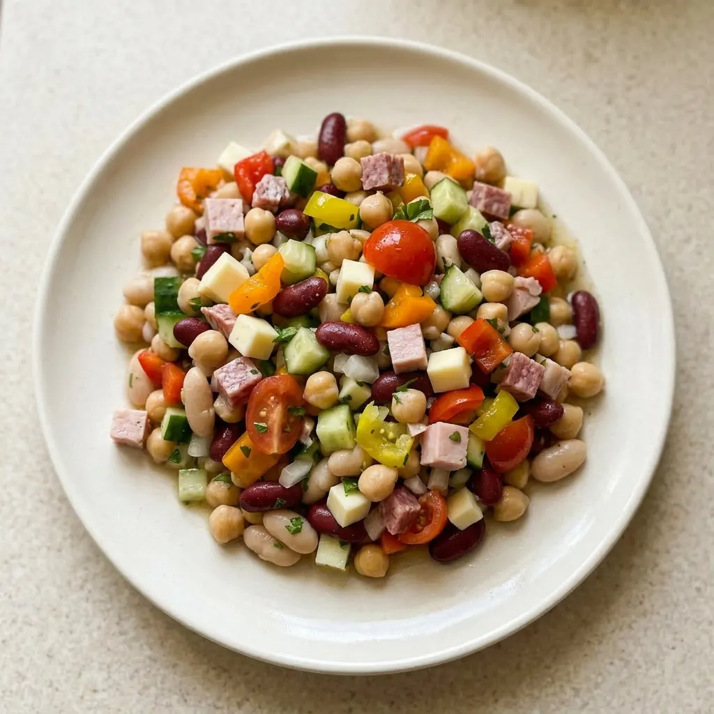 A serving of dense bean salad with chickpeas, cannellini, kidney beans, cucumber, sweet onion, cherry tomatoes, bell peppers, banana peppers, provolone, turkey, and salami.