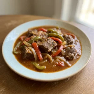 Bird's-eye view of beef stew with sofrito, red and green bell peppers, and onions in a rich brown sauce.