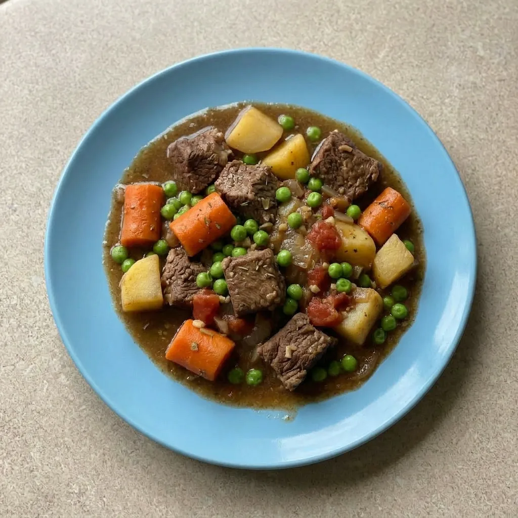 Ready to serve: a bowl of beef stew with beef, carrots, onions, potatoes, and peas in brown broth.