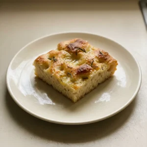 Top-down look at a round focaccia with dimpled surface, topped with fresh rosemary leaves and coarse sea salt.