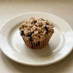 Top-down look at a blueberry muffin with a domed top, scattered cinnamon specks, and visible berry pieces.