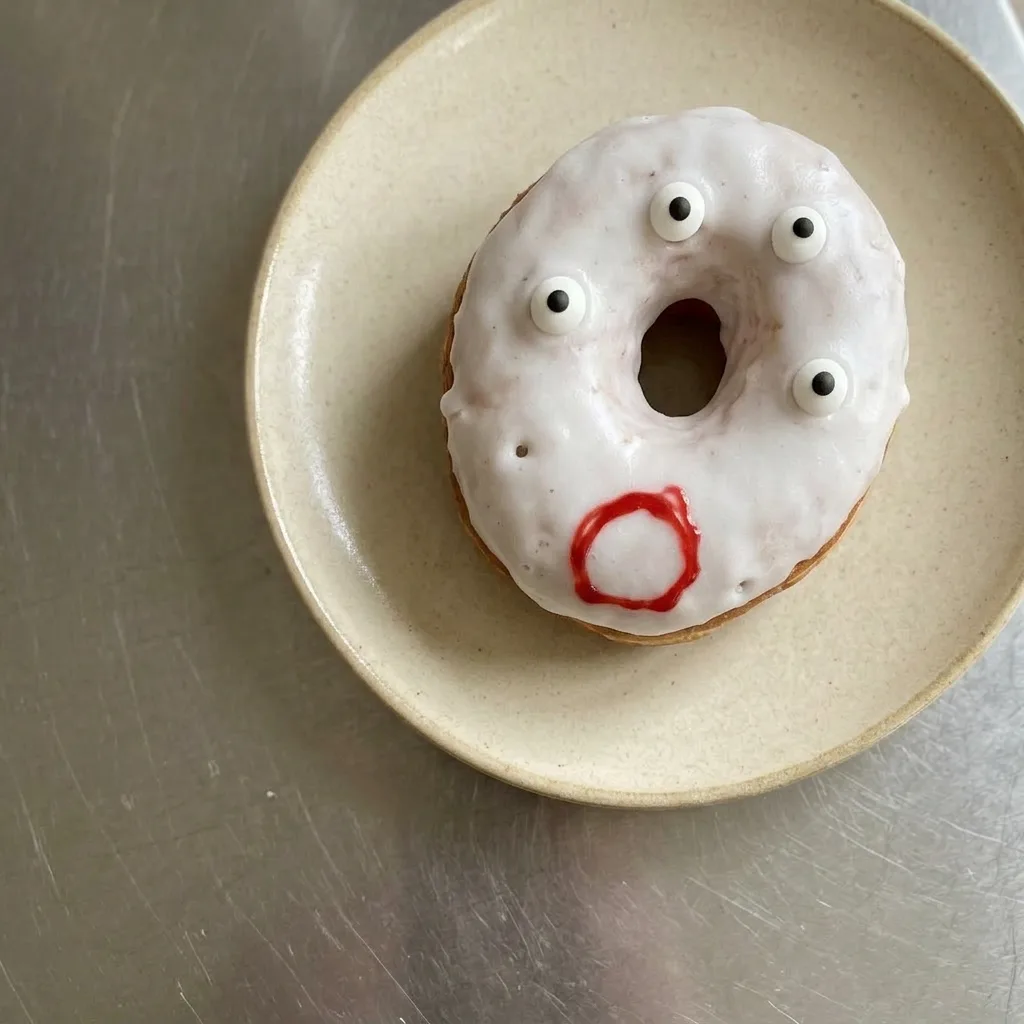 Plated ghost donuts with white icing, candy eyes, and powdered sugar on top.