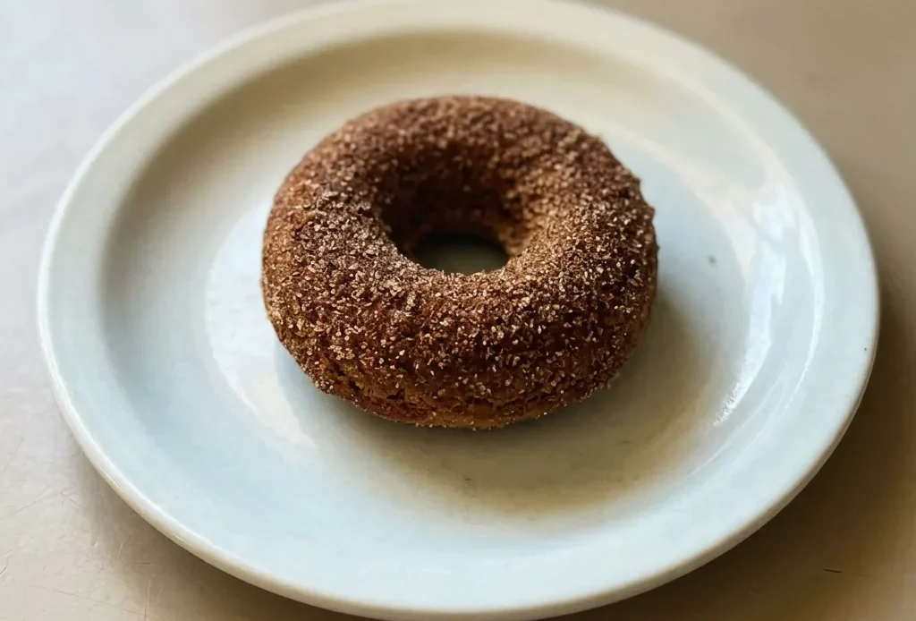 Bird's-eye view of three ring-shaped baked donuts dusted with cinnamon sugar on a dark surface.