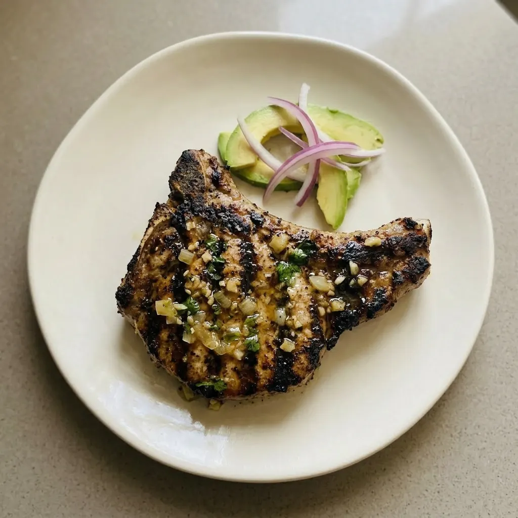 A plate of grilled mojo pork chops topped with garlic, oregano, cumin, and cilantro.