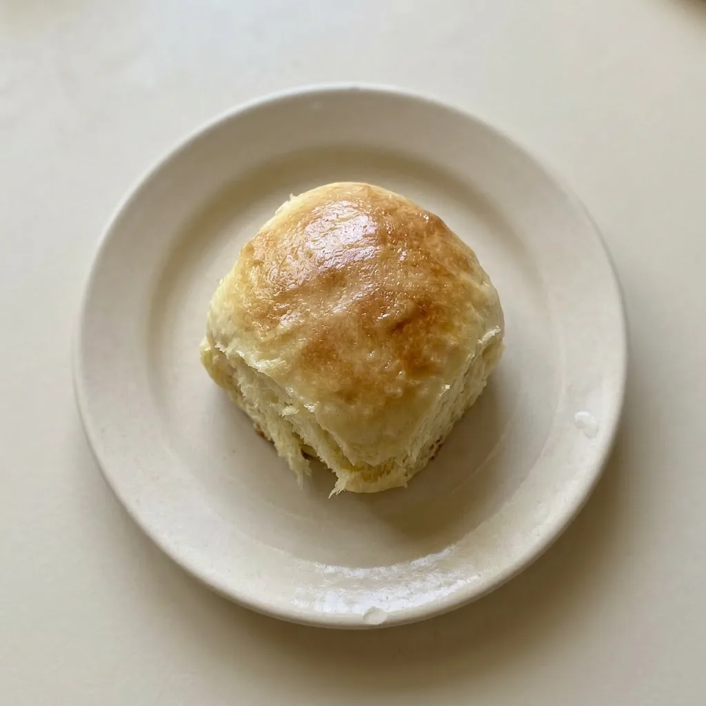 A plate of four Hawaiian rolls, lightly browned and glazed, with a pat of butter melting on one roll, highlighting the sweet, buttery finish.
