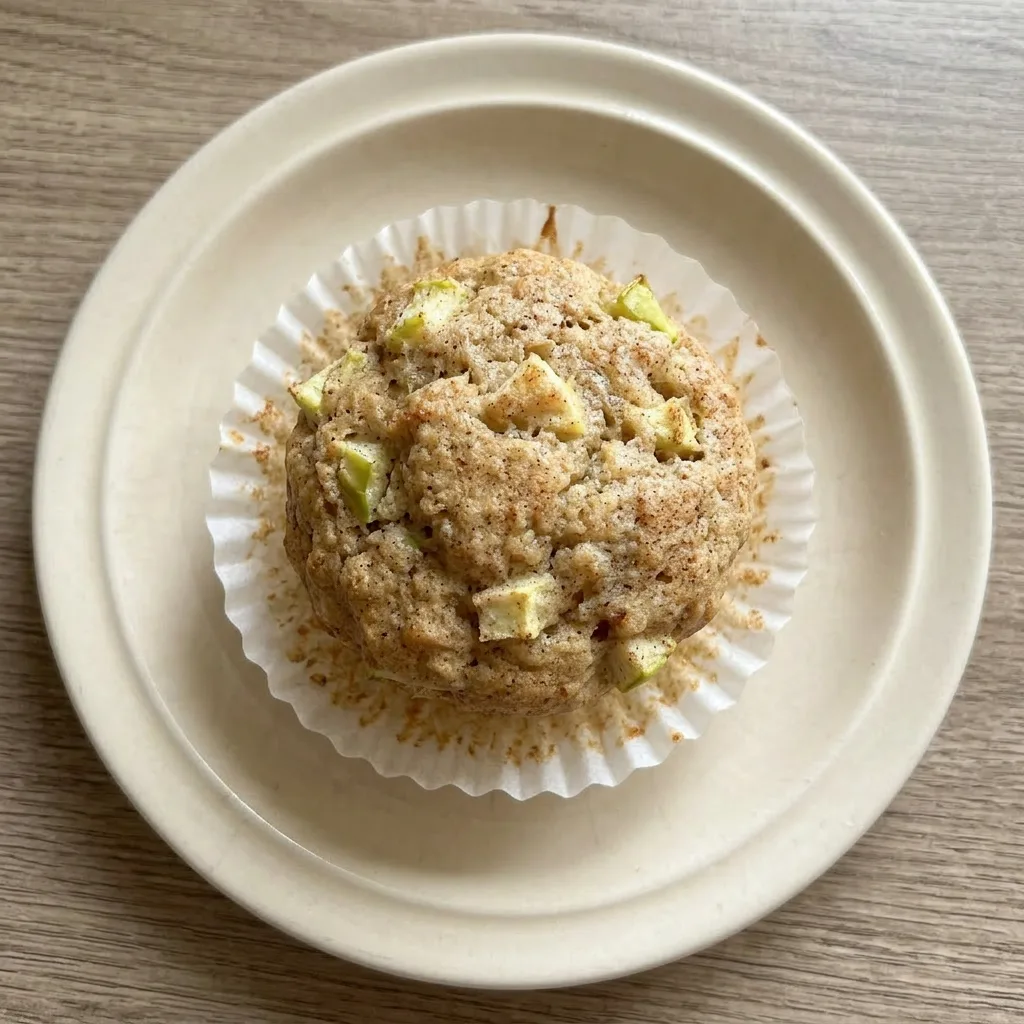A plate of three apple cinnamon muffins, one cut in half, with a side of Greek yogurt and a drizzle of maple syrup.