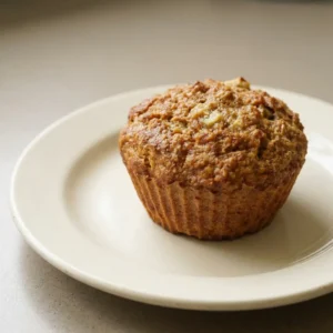 Top-down look at a banana oatmeal muffin with visible oat texture and a slice of banana on top, shot from above.
