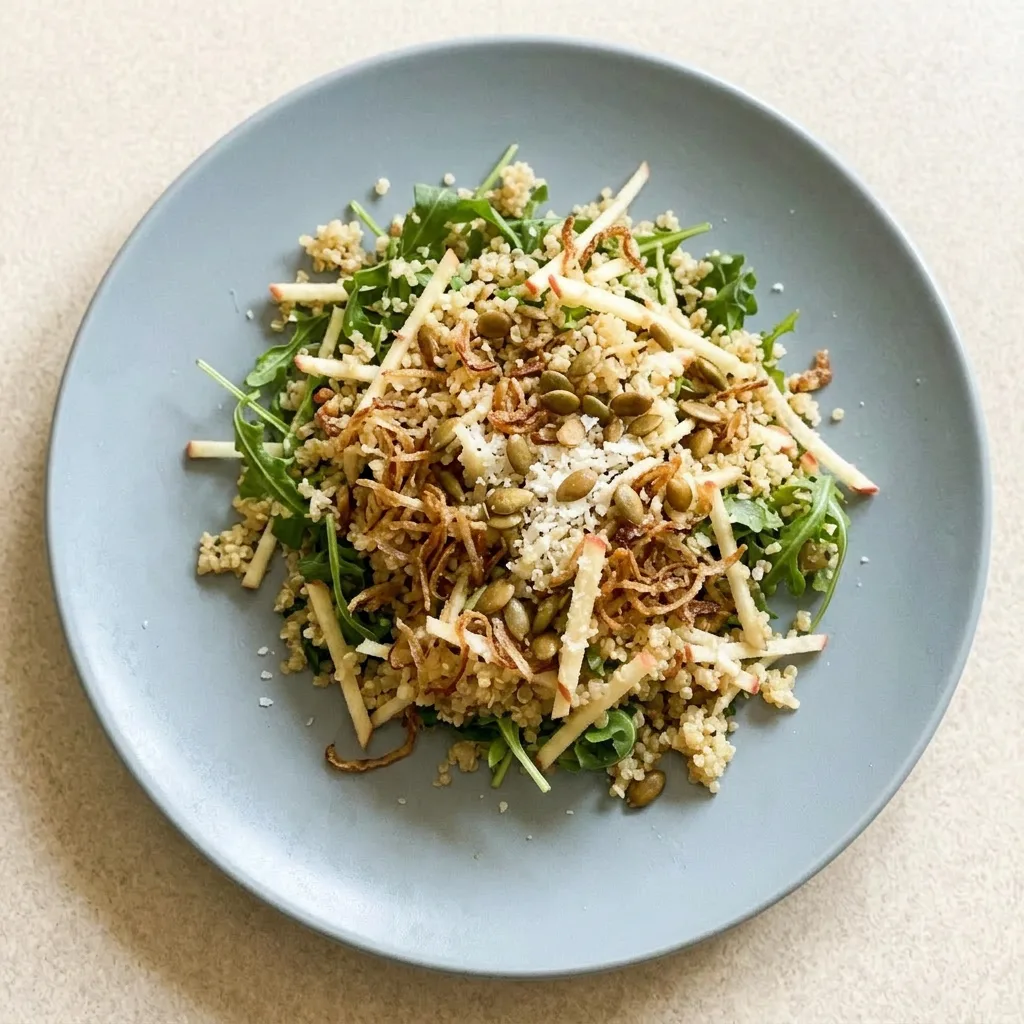 A plate of honey mustard quinoa apple salad with arugula, topped with crispy shallots and apple pieces.