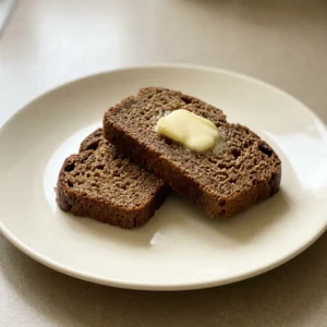 Overhead shot of a dark brown round loaf with a cracked top, sliced into wedges on a dark surface.