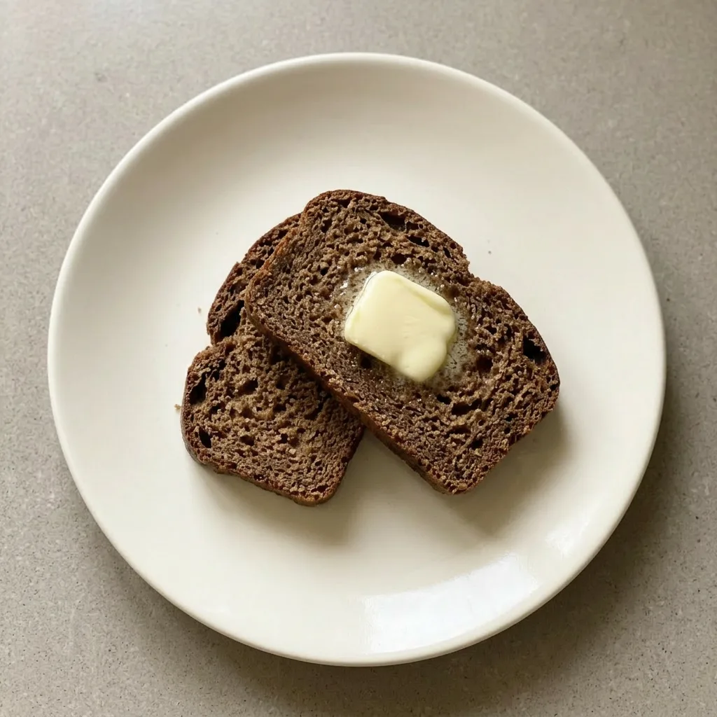 Plated wedge of brown bread with a pat of melting butter on top.