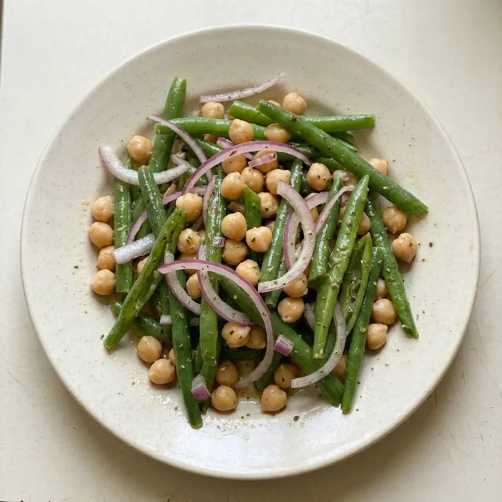 A plate of green bean salad with chickpeas, red onion, and fresh parsley, dressed in olive oil and red wine vinegar.