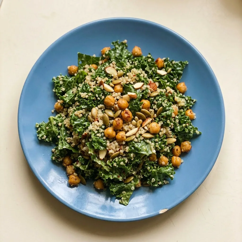 Ready to serve: a mound of kale and quinoa salad garnished with chickpeas, pumpkin seeds, and almonds, with a lemon wedge and a drizzle of dressing.