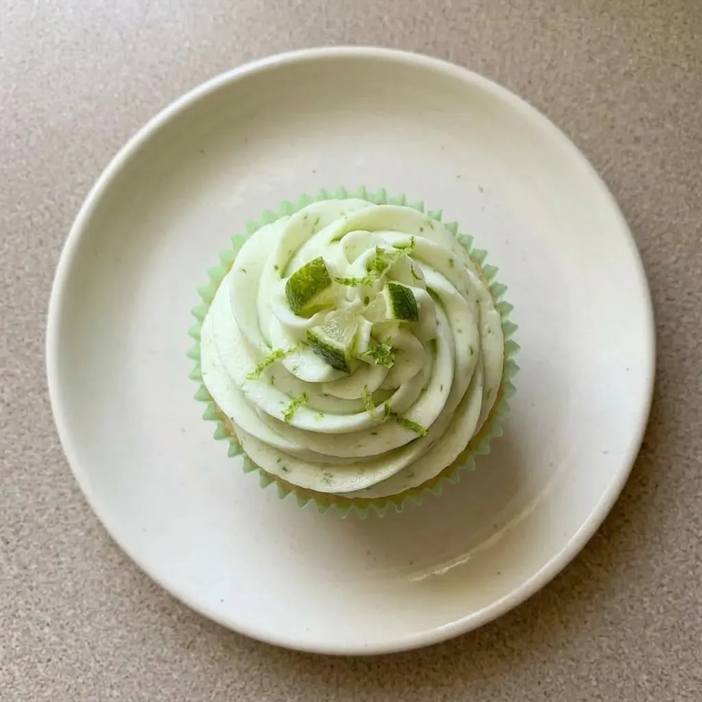 A serving of key lime cupcakes topped with powdered sugar buttercream and fresh lime zest.