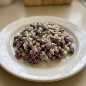 Looking down at a white bowl of kidney bean salad with red beans, chopped celery, and onion, coated in creamy mayonnaise.