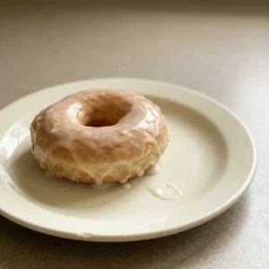 Overhead shot of three glazed doughnuts with glossy white icing on a dark surface.