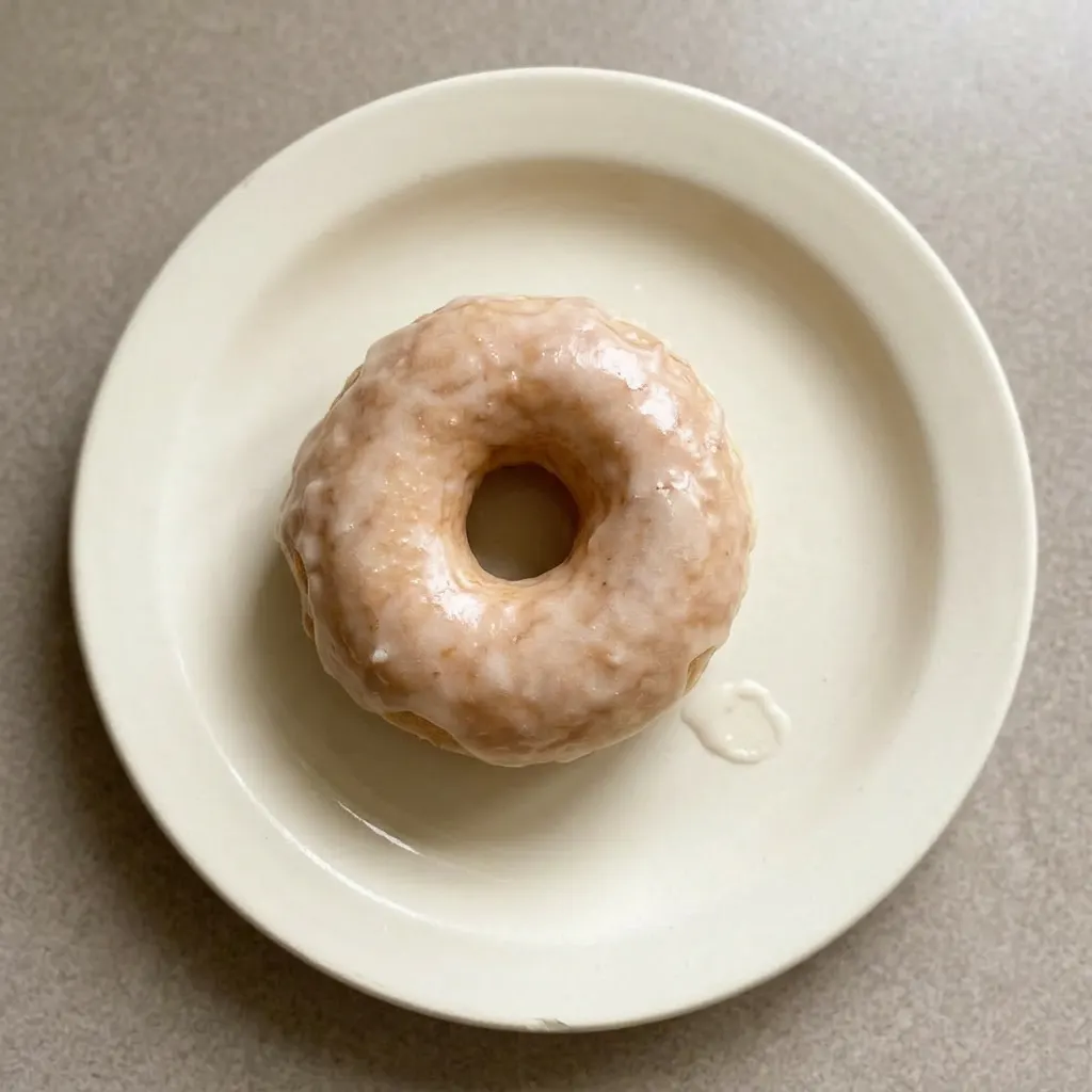 Plated glazed doughnuts with a shiny, translucent icing coating the top.