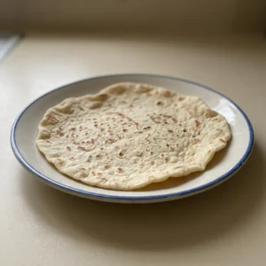 Overhead shot of a round lavash bread with a golden-brown crust and small air bubbles, topped with honey and a dusting of bread flour.