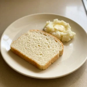 Looking down at a round loaf with a golden crust, scored with a cross pattern, on a dark surface.