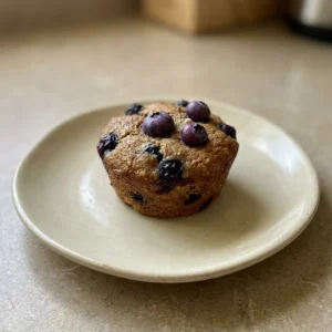 Looking down at three blueberry muffins on a plate, each topped with a few whole blueberries and a sprinkle of almond flour.