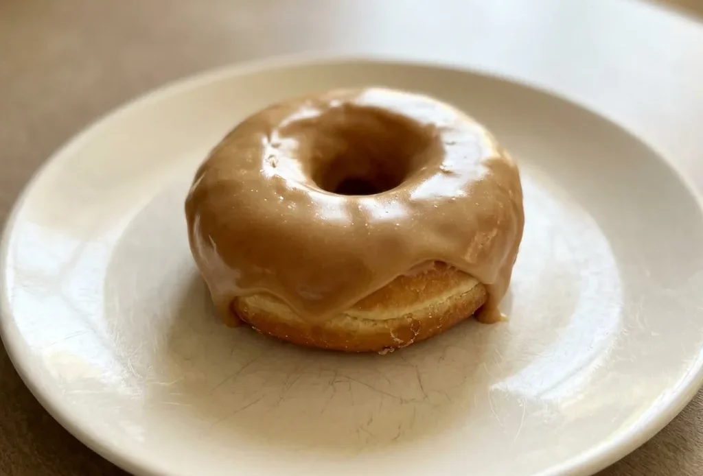 Overhead shot of a round pastry with glossy maple glaze, drizzled lines, and speckles of powdered sugar.