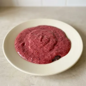 Looking down at a tall glass of purple smoothie topped with a few whole frozen berries and a banana slice.