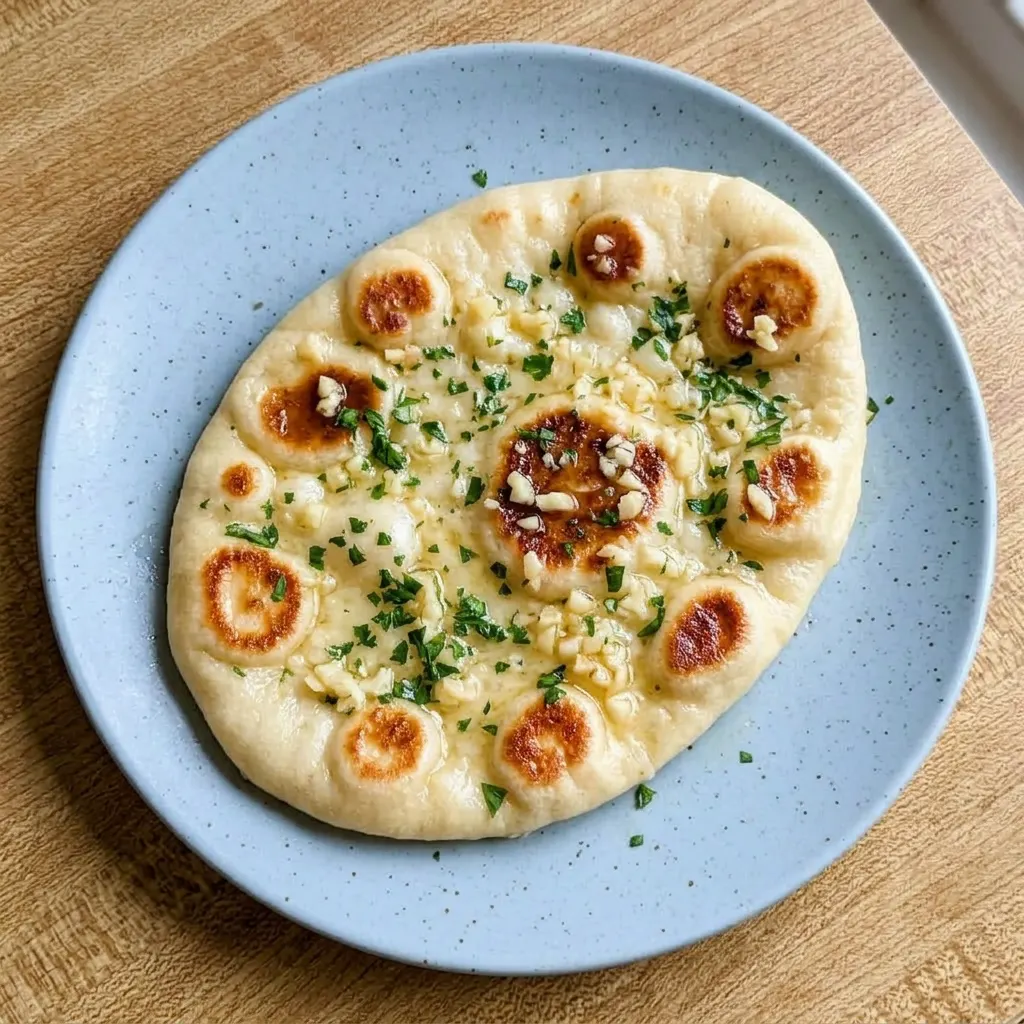Plated naan bread topped with butter and garlic, resting on a dark surface.