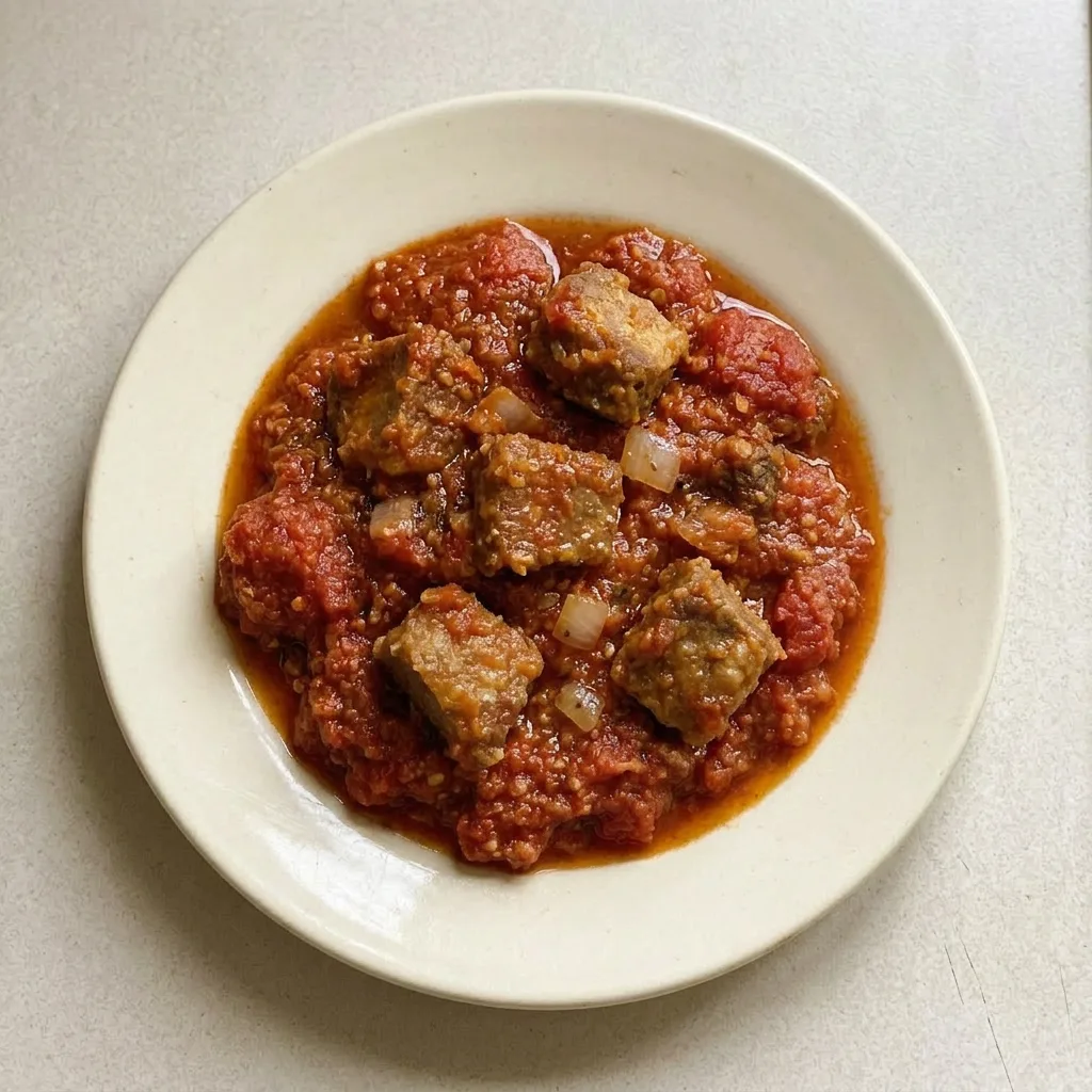 Ready to serve: a ladleful of beef stew with tomato and pepper bits, garnished with curry and bouillon.