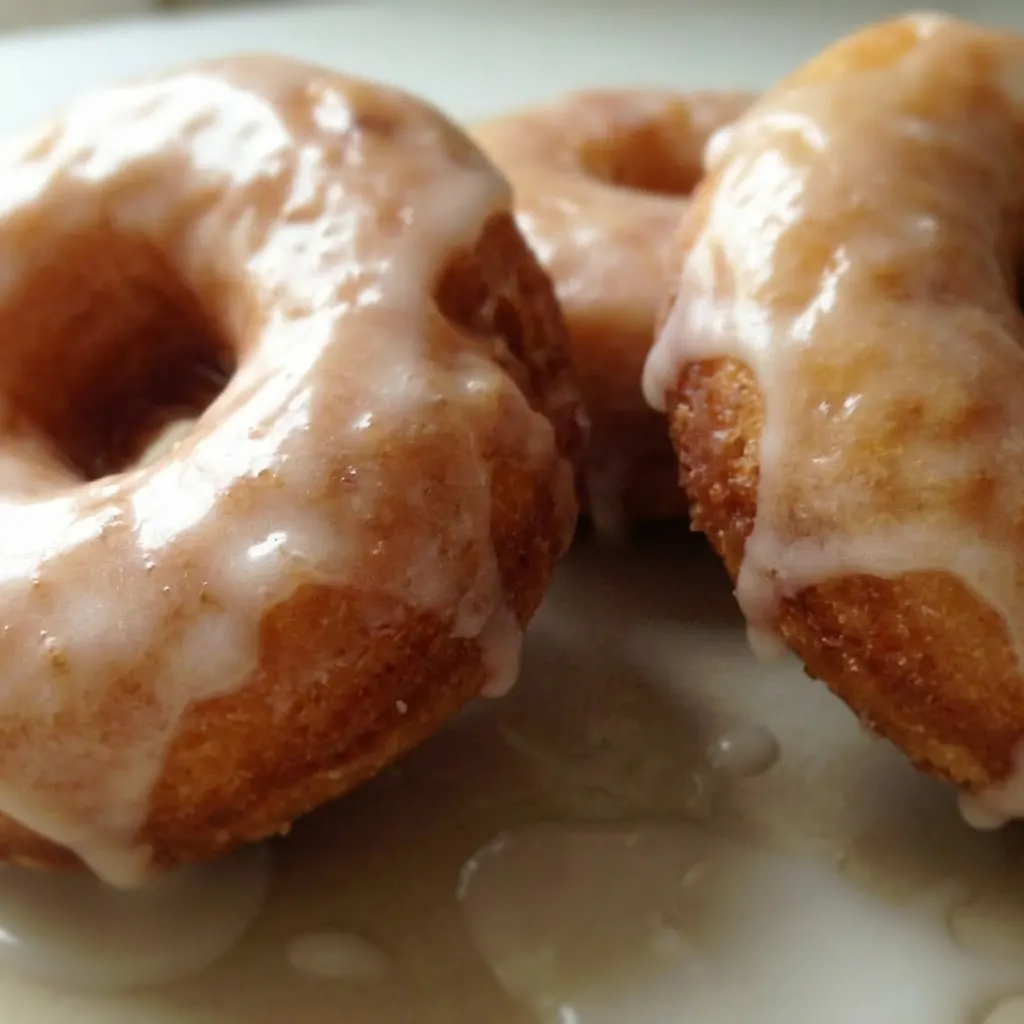 Close view of a donut with glossy white glaze and visible butter and milk in the dough.